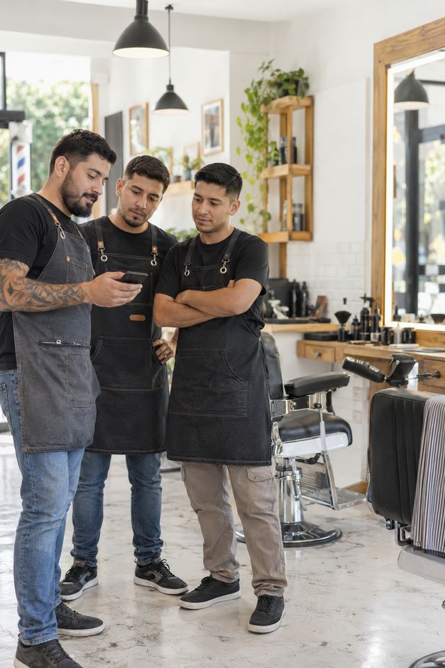 Tres barberos mirando el celular en su barbería